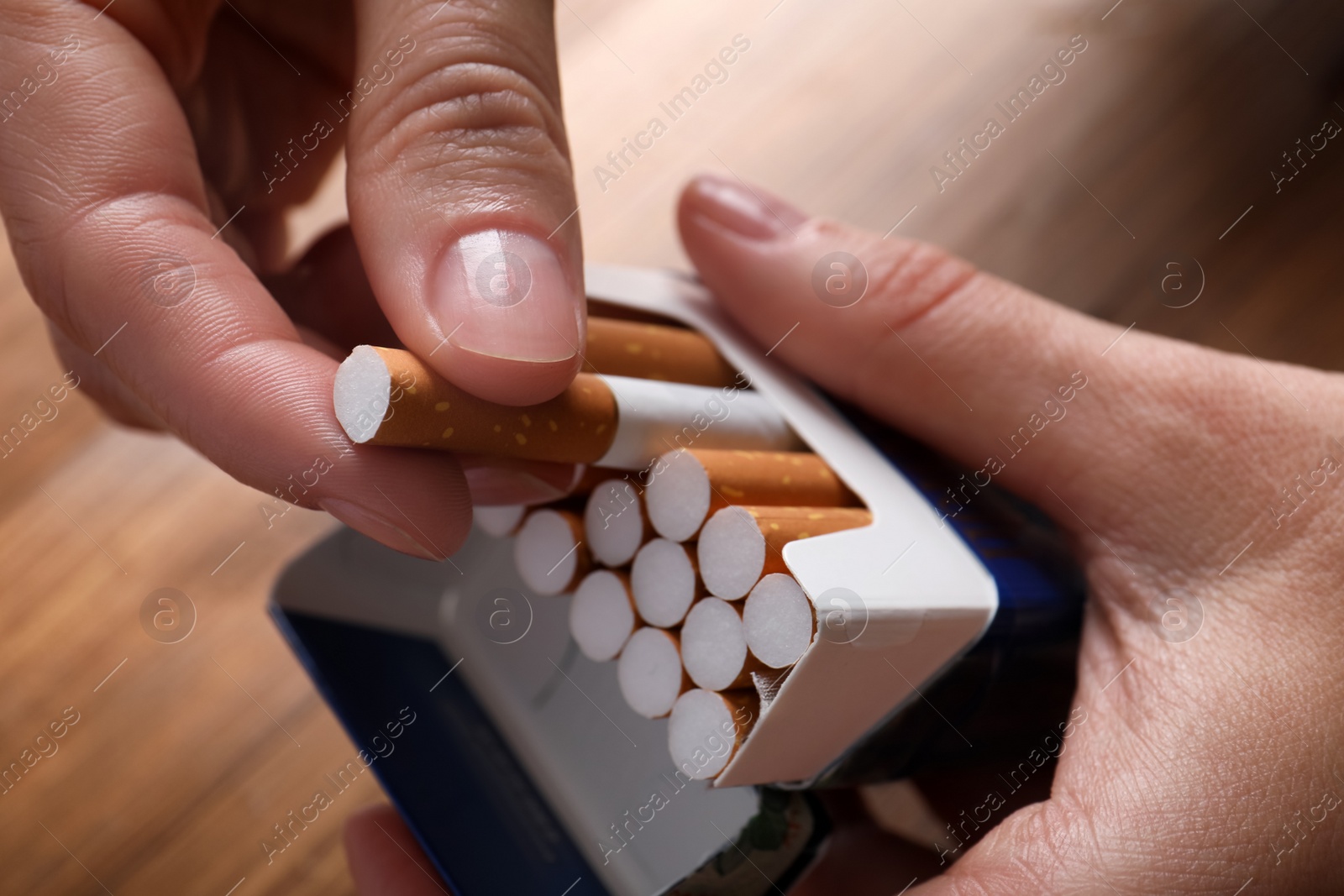 Photo of Woman taking cigarette out of pack at wooden table, closeup