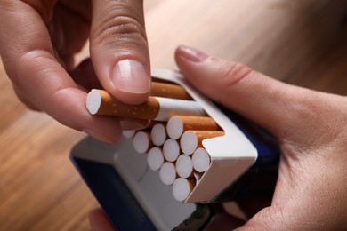 Photo of Woman taking cigarette out of pack at wooden table, closeup