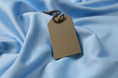Photo of Blank grey tag on light blue silky fabric, closeup. Space for text