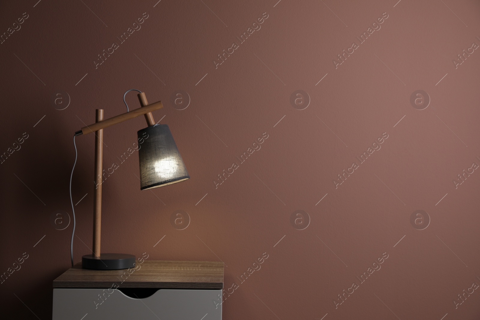 Photo of Wooden nightstand with lamp in room, space for text