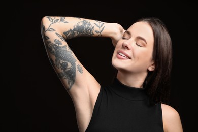 Photo of Beautiful woman with tattoos on arm against black background