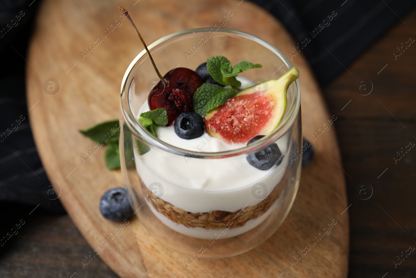 Photo of Glass with yogurt, berries, mint and granola on wooden table, closeup