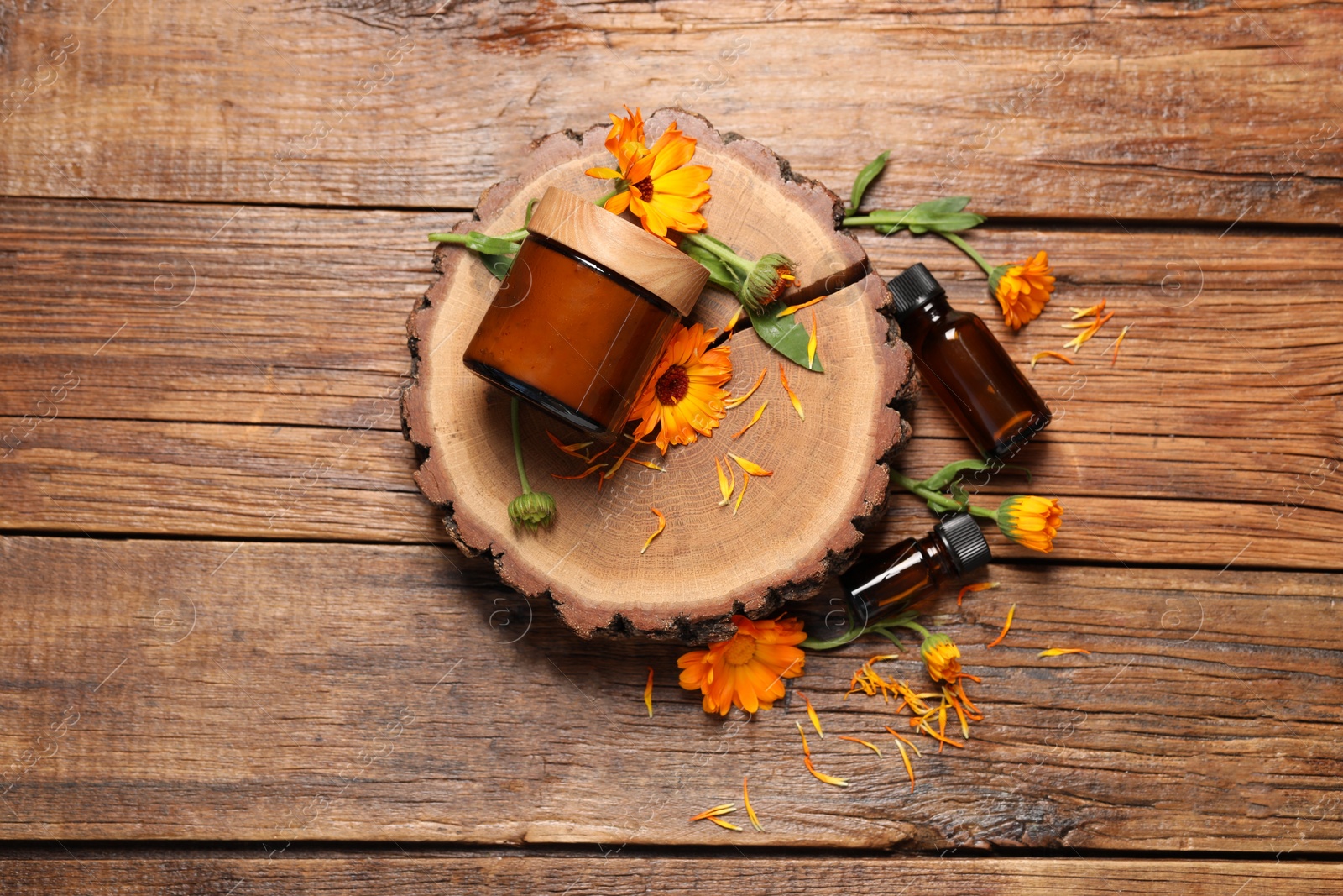 Photo of Different cosmetic products and beautiful calendula flowers on wooden table, flat lay