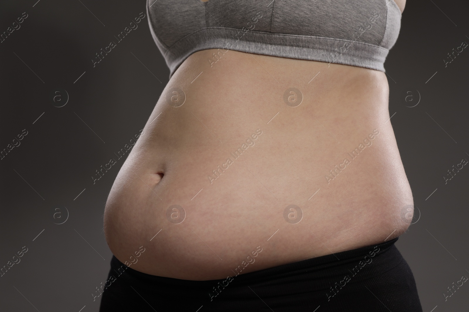 Photo of Woman with excessive belly fat on grey background, closeup. Overweight problem