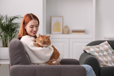 Happy woman with her cute cat in armchair at home. Space for text