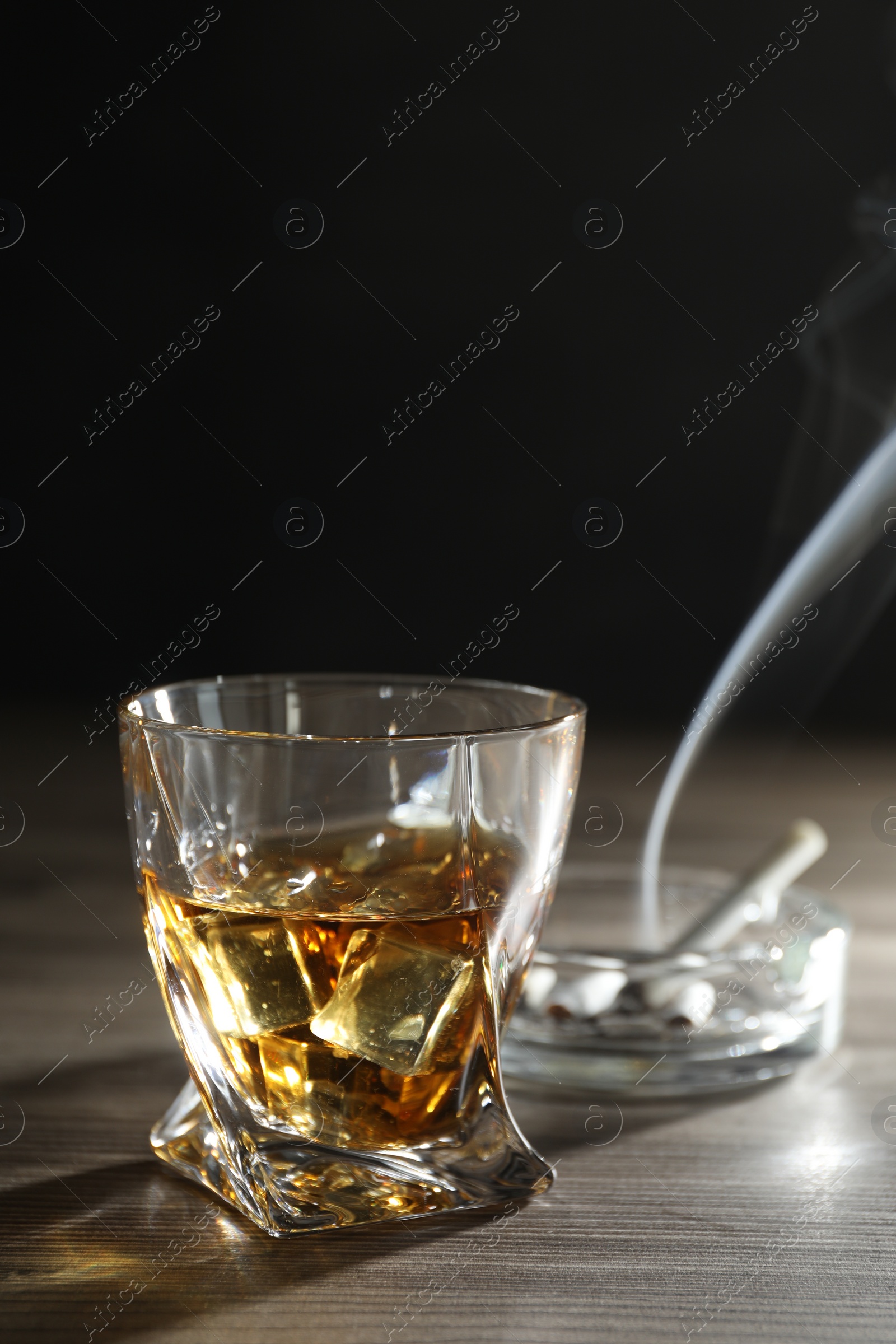 Photo of Alcohol addiction. Whiskey in glass, cigarettes and ashtray on wooden table