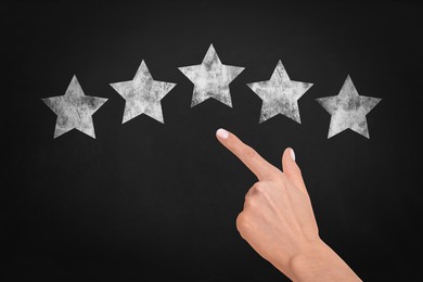 Image of Quality rating. Woman pointing at chalked stars on blackboard, closeup