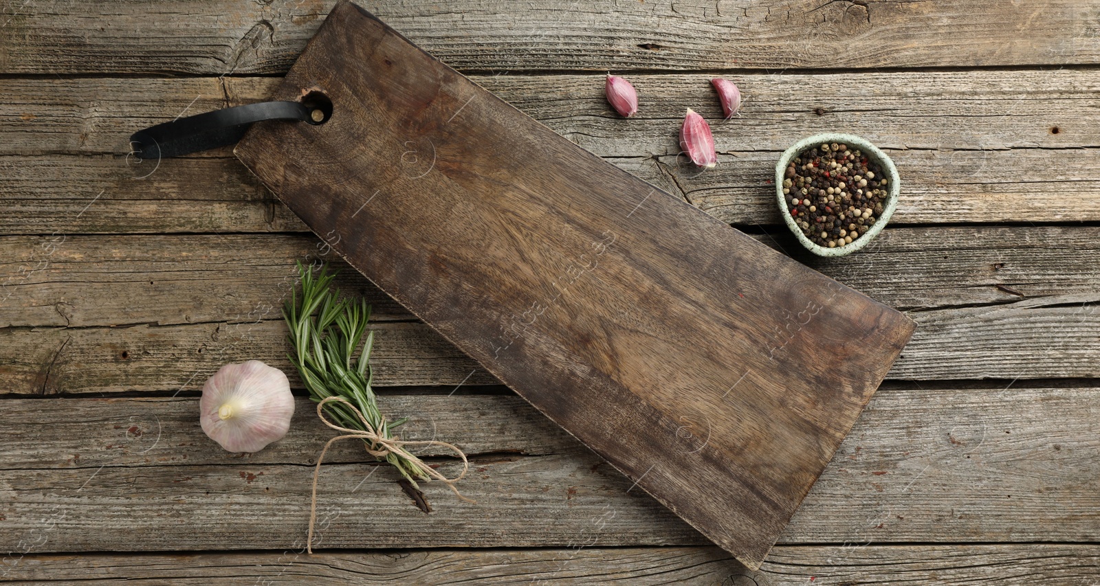 Photo of Cutting board, garlic, pepper and rosemary on wooden table, flat lay. Space for text