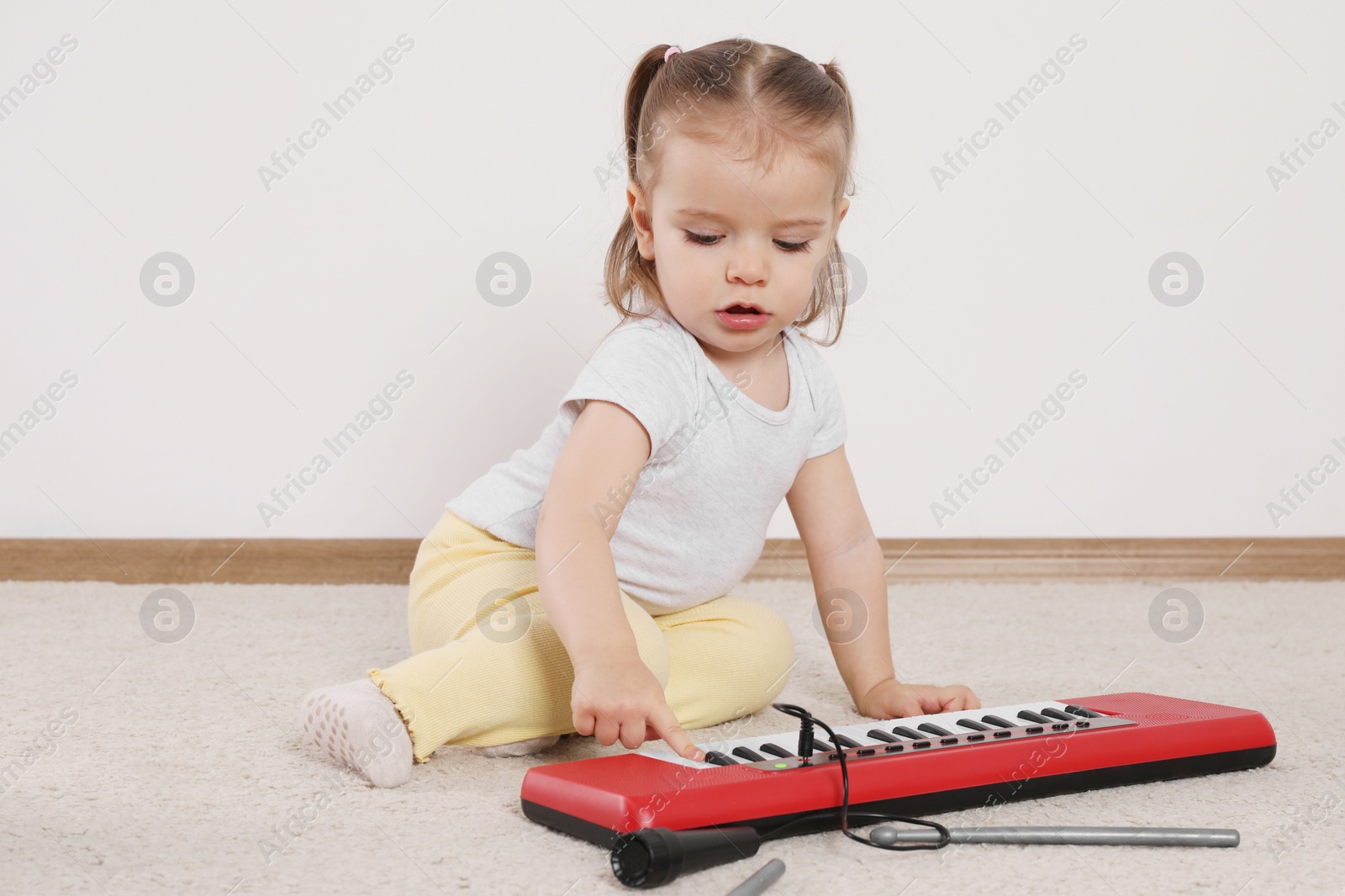 Photo of Cute little girl playing with toy piano at home