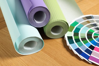 Photo of Different wallpaper rolls and color palette samples on wooden table