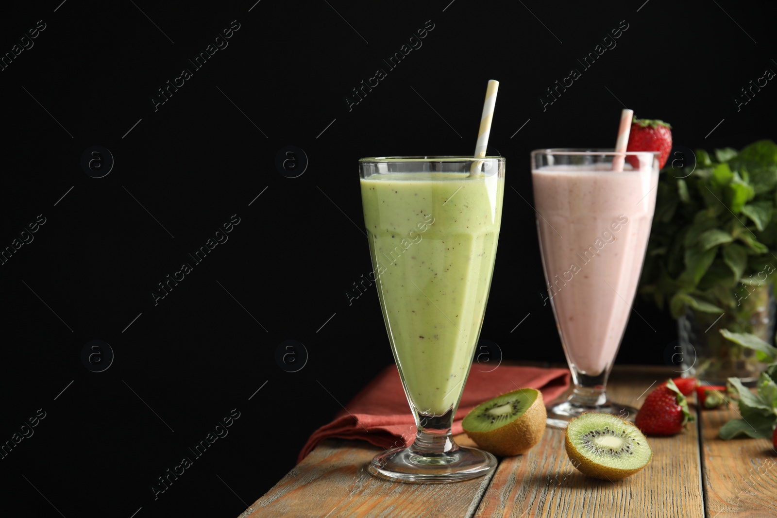 Photo of Tasty kiwi and strawberry milk shakes on wooden table against black background, space for text