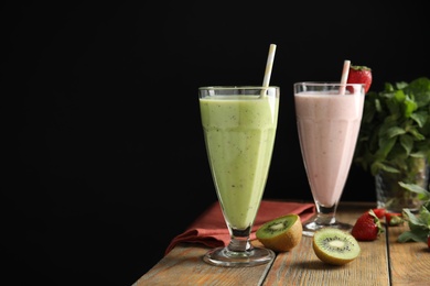 Photo of Tasty kiwi and strawberry milk shakes on wooden table against black background, space for text