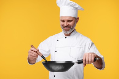 Photo of Happy chef in uniform with wok and spoon on orange background