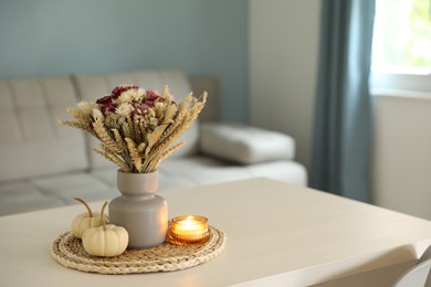 Beautiful bouquet of dry flowers, small pumpkins and candle on white table indoors, space for text