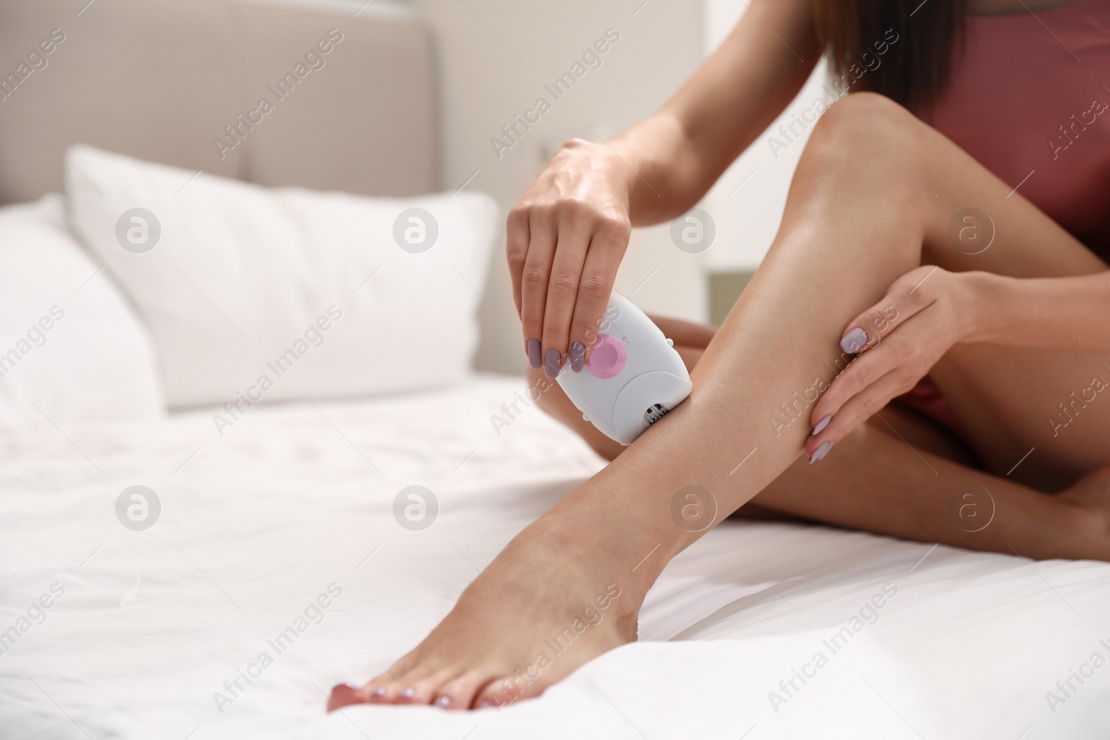 Photo of Young woman epilating her legs in bedroom, closeup