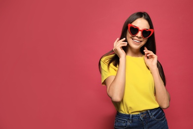 Portrait of beautiful young woman with heart shaped sunglasses on color background. Space for text