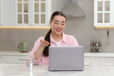 Photo of Woman having video chat via laptop at white table in kitchen