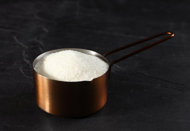 Photo of Metal measuring scoop of granulated sugar on black table