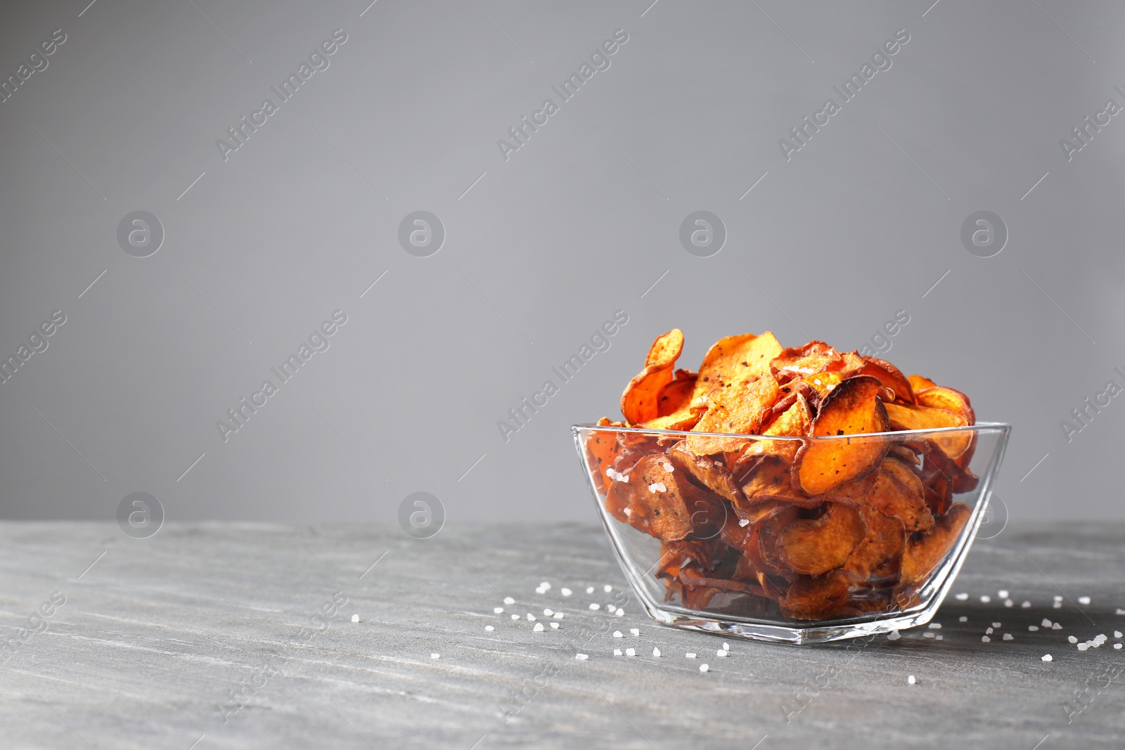 Photo of Bowl of sweet potato chips and salt on table against grey background. Space for text