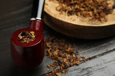 Smoking pipe with dry tobacco on dark wooden table, closeup. Space for text