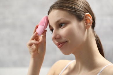 Washing face. Young woman with cleansing brush indoors