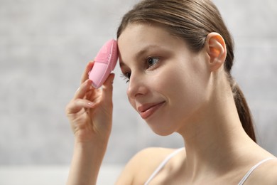 Photo of Washing face. Young woman with cleansing brush indoors