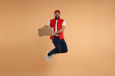Photo of Happy young courier jumping with parcel on light brown background