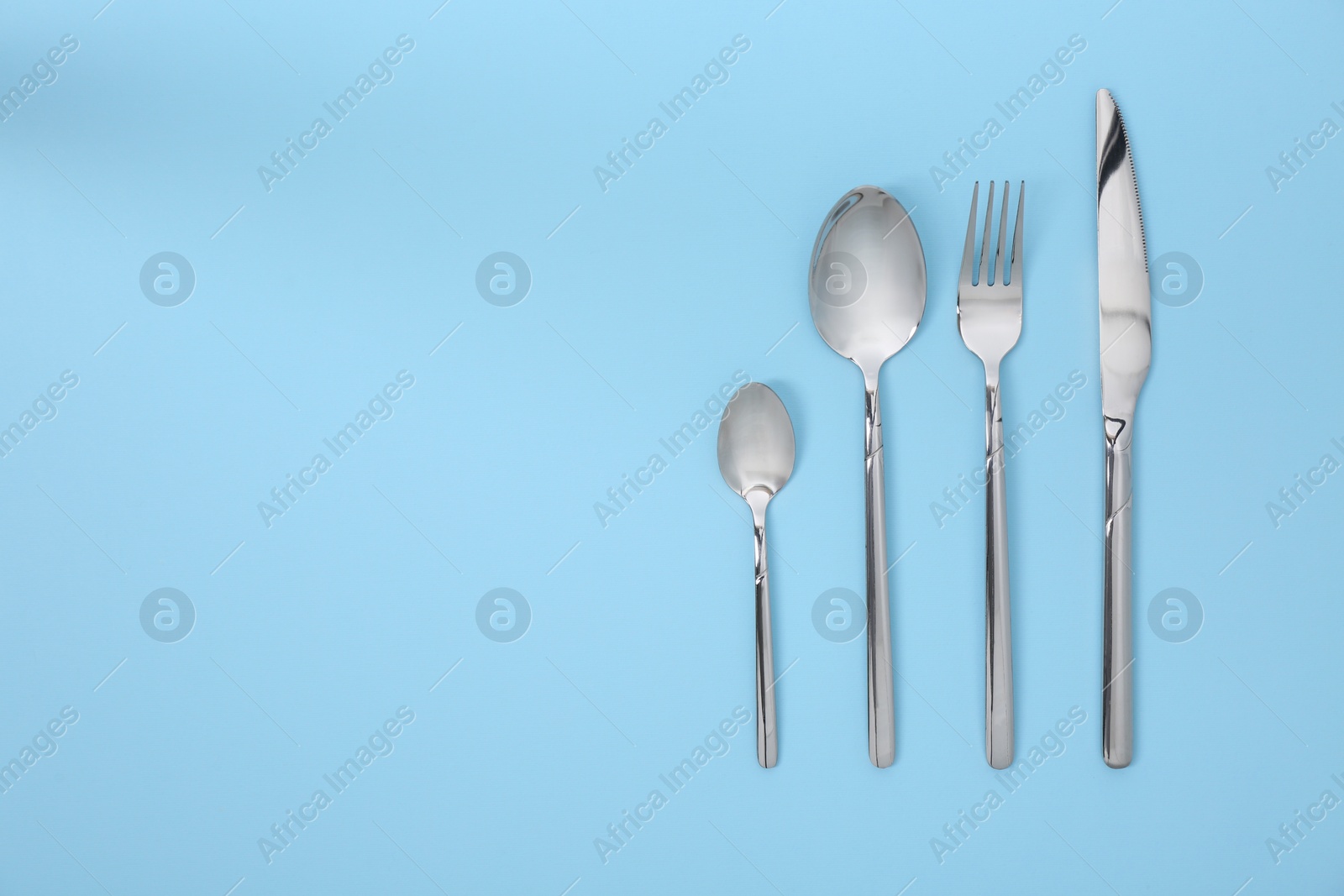 Photo of Stylish silver cutlery set on light blue background, flat lay. Space for text