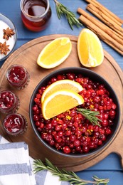 Cranberries in bowl, jars with sauce and ingredients on blue wooden table, flat lay