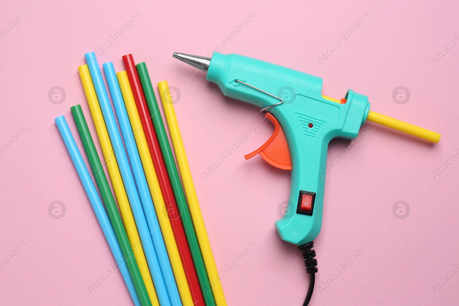Photo of Turquoise glue gun and colorful sticks on pink background, flat lay