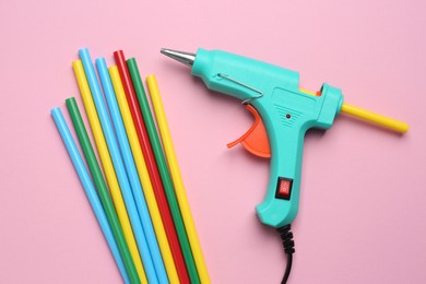 Photo of Turquoise glue gun and colorful sticks on pink background, flat lay