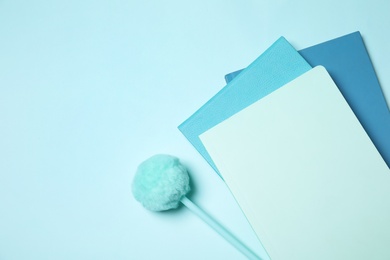 Photo of Pen with pompom and notebooks on light blue background, flat lay. Space for text