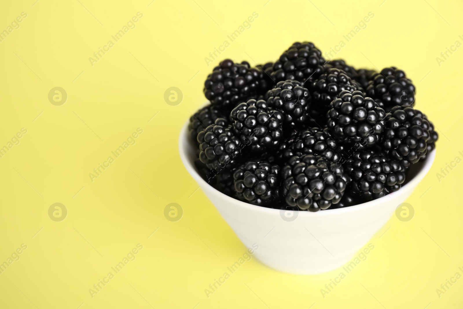 Photo of Fresh ripe blackberries in bowl on yellow background. Space for text