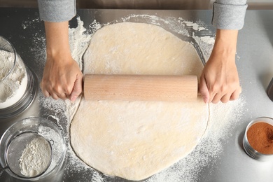 Photo of Woman rolling dough for cinnamon rolls on table, top view