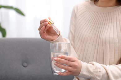 Photo of Woman dripping food supplement into glass of water indoors, closeup. Space for text