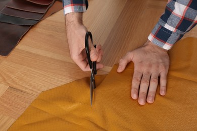Photo of Man cutting orange leather with scissors at wooden table, closeup