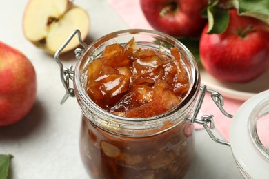 Photo of Tasty apple jam in glass jar and fresh fruits on table. closeup
