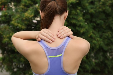 Photo of Young woman suffering from neck pain outdoors, back view