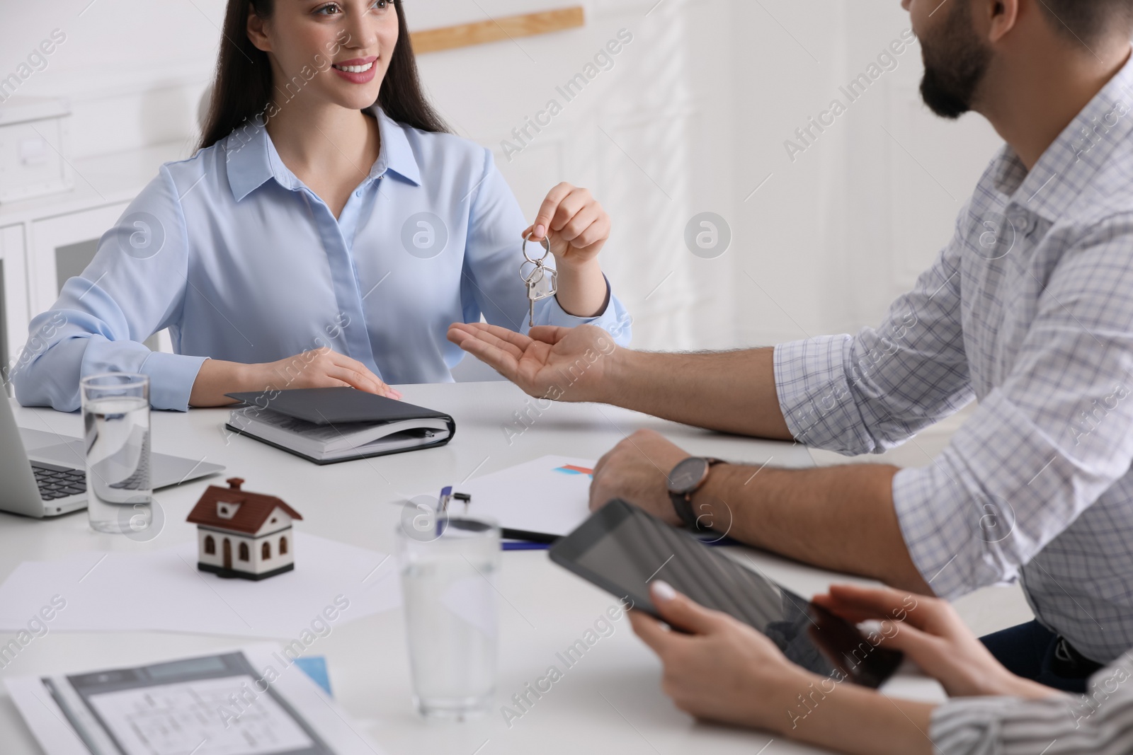 Photo of Real estate agent giving house key to young couple in office, closeup. Mortgage concept