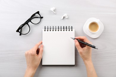 Woman with notebook and pen at white wooden table, top view. Space for text