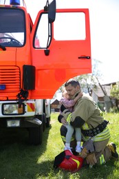 Photo of Firefighter in uniform with rescued little girl near fire truck outdoors. Save life