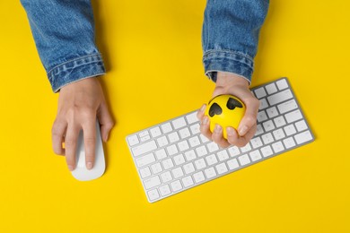 Woman squeezing antistress ball while working with computer on yellow background, top view