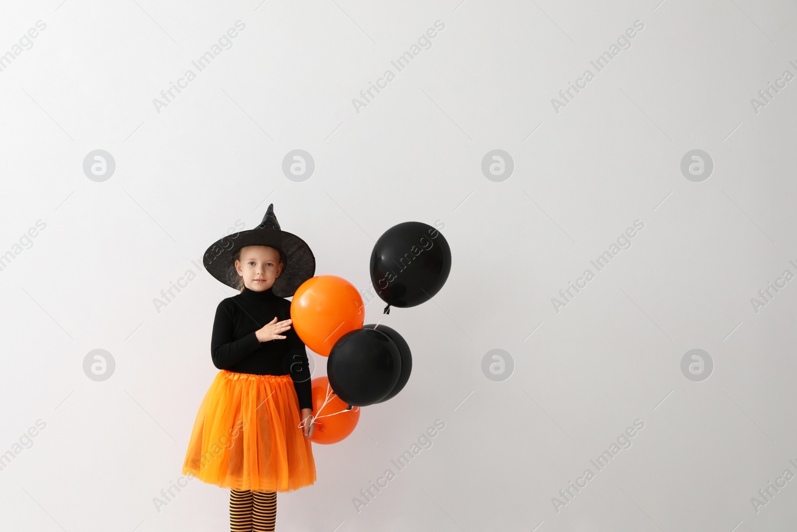 Photo of Cute little girl with balloons wearing Halloween costume on light background. Space for text