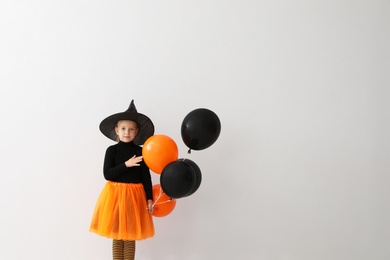 Cute little girl with balloons wearing Halloween costume on light background. Space for text