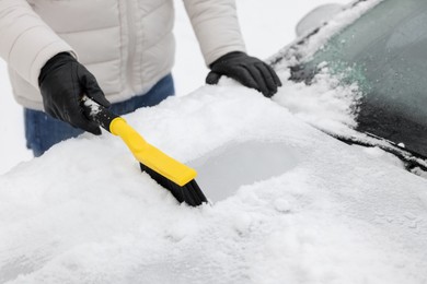 Photo of Man cleaning snow from car hood outdoors, closeup