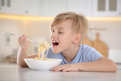 Photo of Happy boy eating tasty pasta at table in kitchen