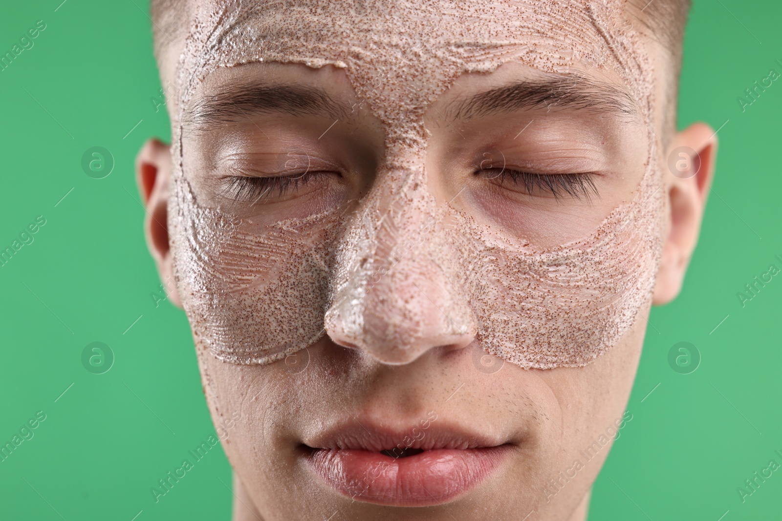 Photo of Handsome man with facial mask on his face against green background, closeup