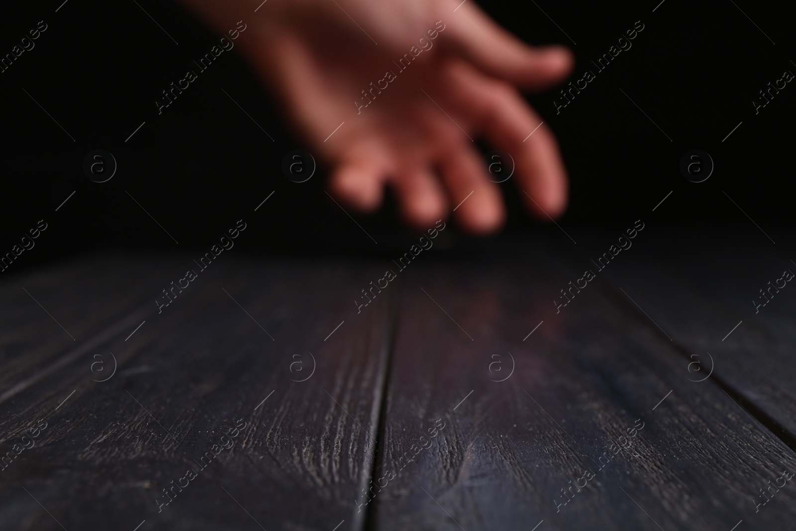 Photo of Man holding hand above black wooden table, selective focus. Space for text