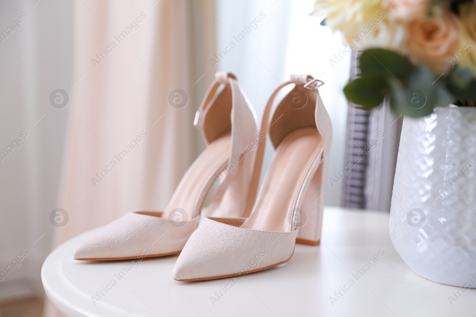 Photo of High heeled shoes on white table and beige dress indoors, closeup