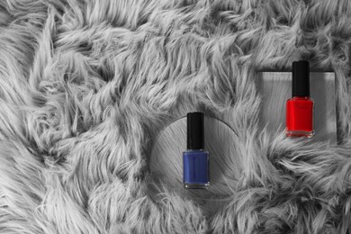 Photo of Bright nail polishes in bottles on grey faux fur, top view. Space for text